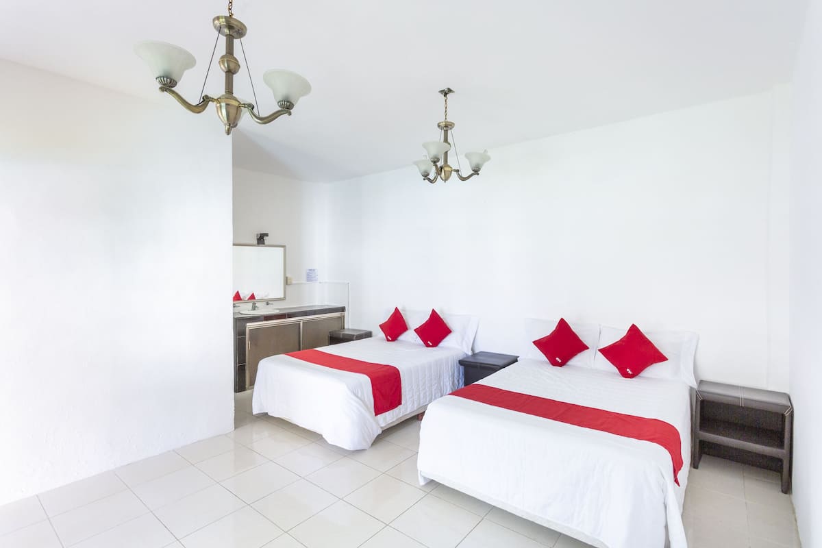 A hotel room with two beds, a chandelier, a small desk, and a mirror.