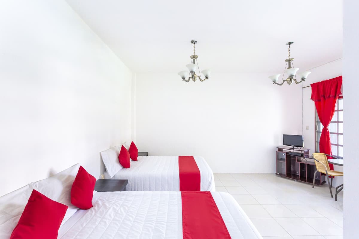 A hotel room with two beds, a desk, a chair, a TV, and a window with red curtains.