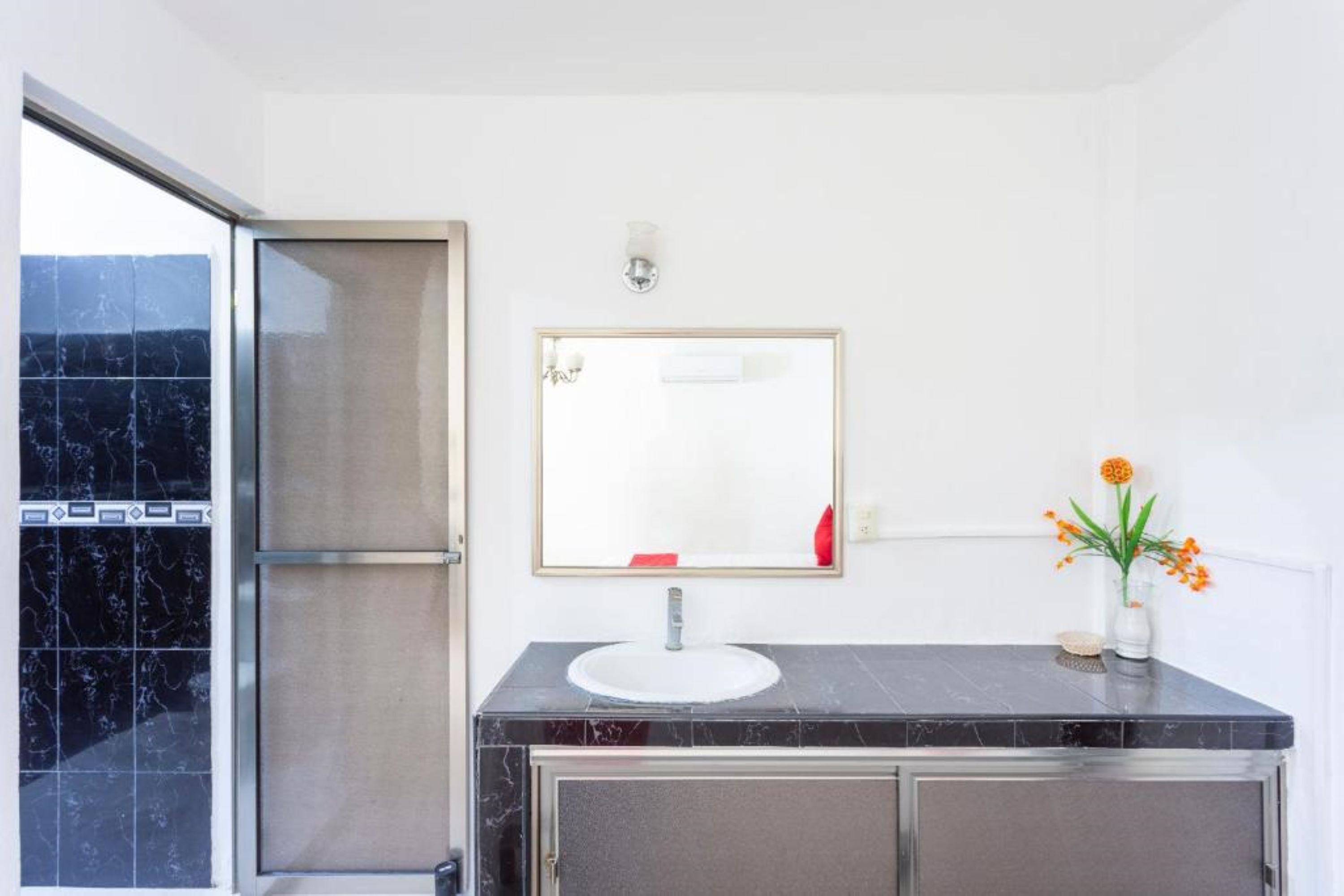 A bathroom with a marble sink, a mirror, and a vase with flowers.