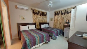A hotel room with two beds, a ceiling fan, an air conditioner, curtains, a coffee machine, and a desk with a remote control. - The Golden Gate Inn (Basseterre)