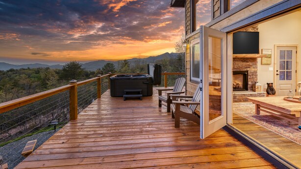 Una terraza de madera con un jacuzzi, sillas y una chimenea de piedra.