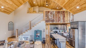 Una cocina amplia con techo alto, vigas de madera, una isla central y electrodomésticos de acero inoxidable.