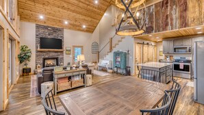 Un salón espacioso con una gran mesa de comedor de madera, chimenea y cocina equipada con electrodomésticos modernos.