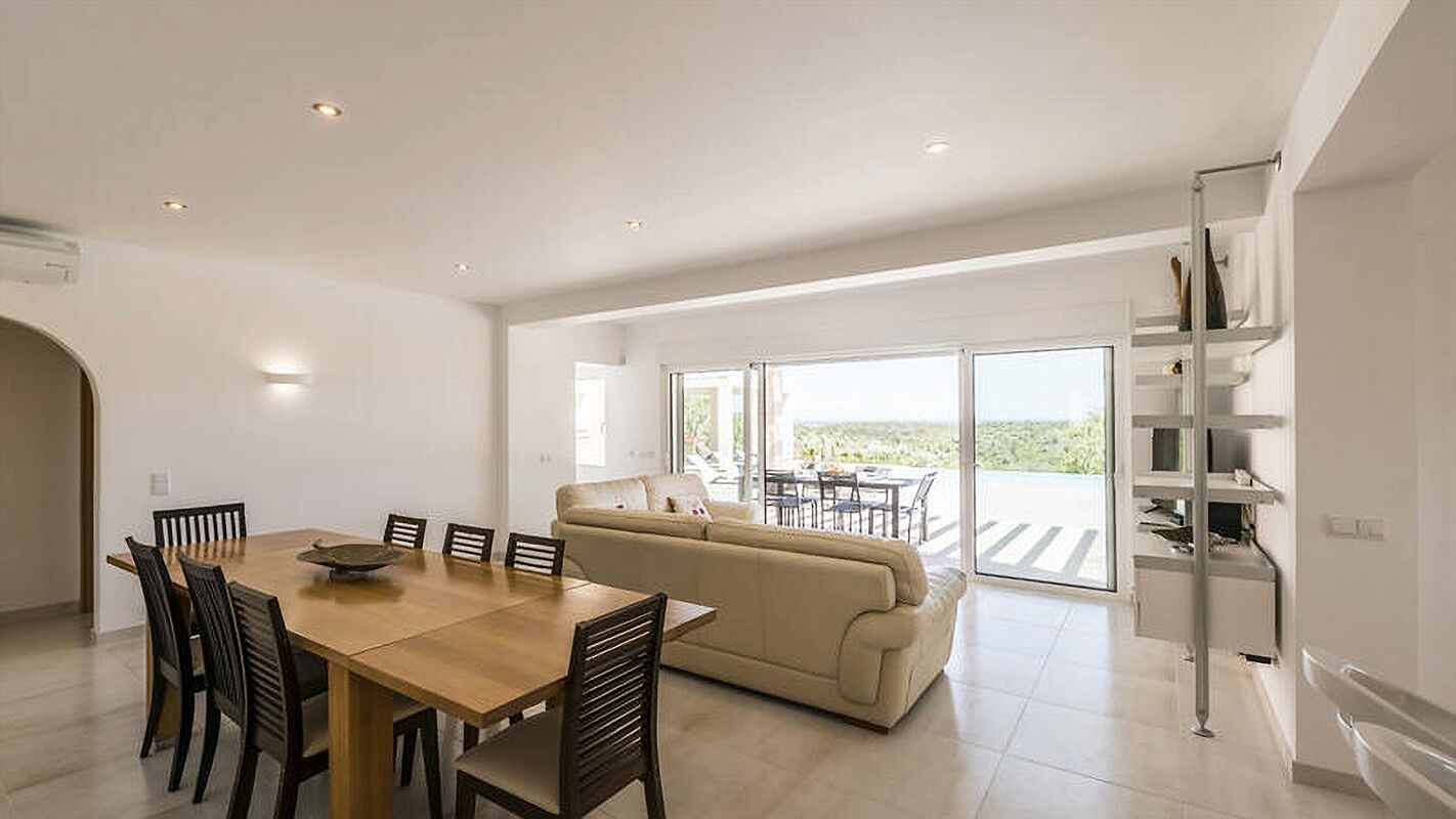 A spacious living area with a dining table, sofa, and a balcony with a view.