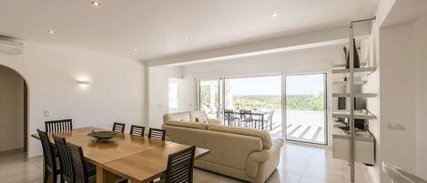 A spacious living area with a dining table, sofa, and a balcony with a view.