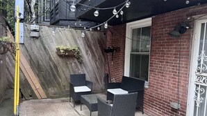 Un patio al aire libre con mobiliario de mimbre, un muro de ladrillo y una valla de madera.