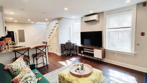 Una sala de estar moderna con un sofá verde, una mesa de centro, un televisor y una escalera que conduce a otro nivel.