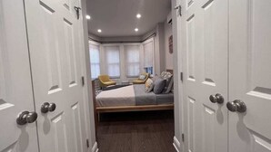 Un dormitorio con cama, ventana con persianas, una silla y un armario.