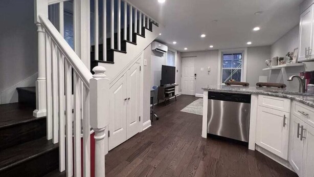 Una cocina moderna con armarios blancos, lavavajillas de acero inoxidable y una escalera de madera.