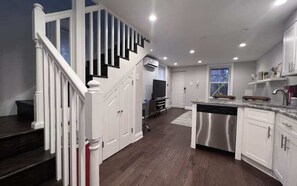 A modern kitchen with white cabinetry, a stainless steel dishwasher, and a wooden staircase. - Charm In Rittenhouse | Patio | Hosted by Stay Rafa (Philadelphia)