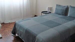 Un dormitorio con cama, mesita de noche, lámpara y ventana con cortinas.