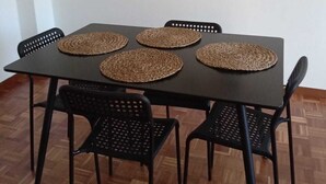Una mesa de comedor con cuatro sillas negras, cada una con un posavasos tejido. La mesa está frente a una pared blanca con arte abstracto.