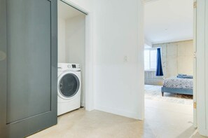 A laundry room with a washing machine, a bedroom with a bed and a window, and a hallway leading to another room. - Modern Townhome 15 | Free Park | Hosted Stay Rafa (Philadelphia)