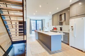A modern kitchen with a central island, wooden staircase, and a view of the city. - Modern Townhome 15 | Free Park | Hosted Stay Rafa (Philadelphia)