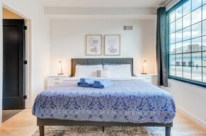 A bedroom with a bed, two bedside tables, a window with curtains, and artwork on the wall.