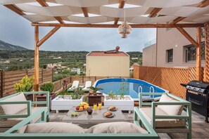 A rooftop terrace with a swimming pool, lounge chairs, and a dining table with fruit and drinks.