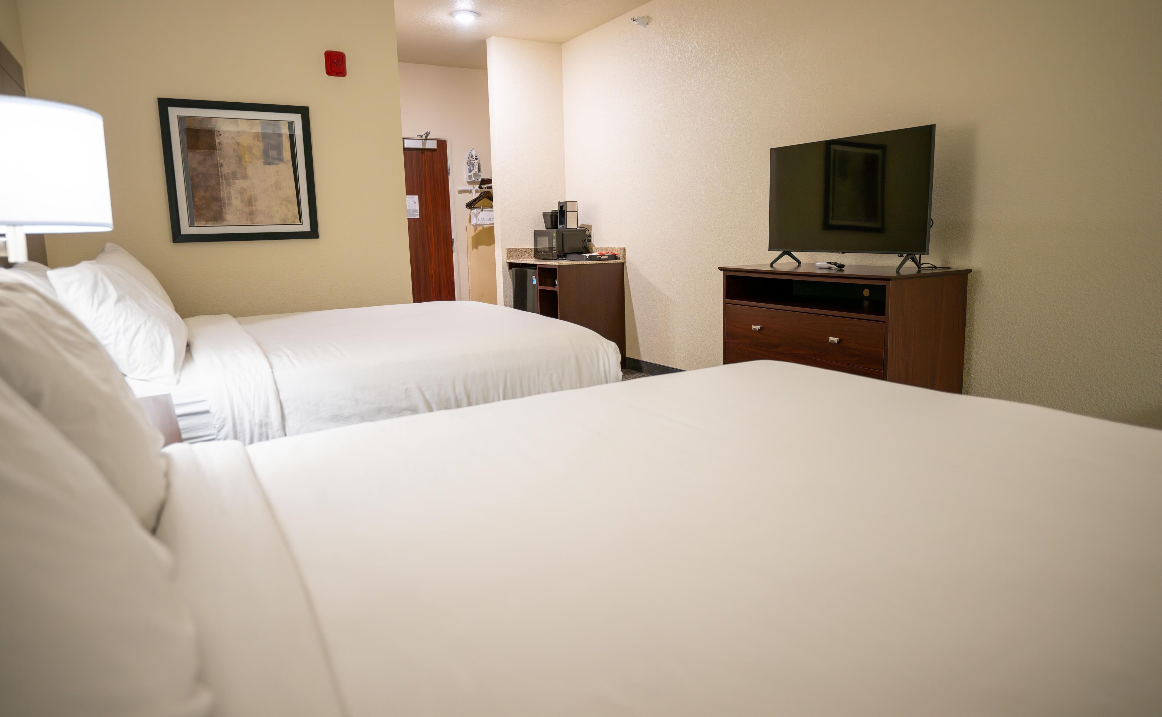 A hotel room with two beds, a desk with a computer, a TV, and a framed picture on the wall.