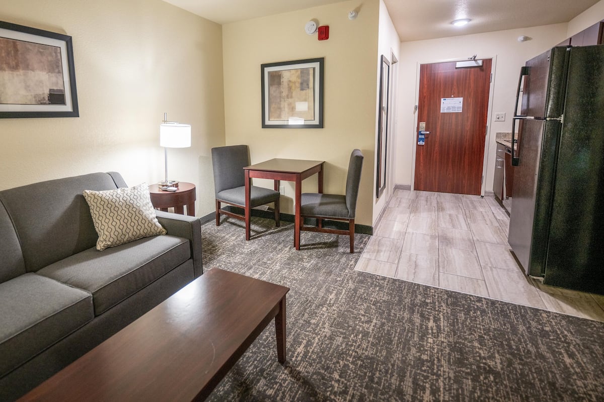 A compact living room with a sofa, a small table, two chairs, and a coffee table. There is a door leading to a kitchen area.