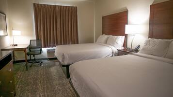 A hotel room with two beds, a desk, a chair, a lamp, and an air conditioning unit.
