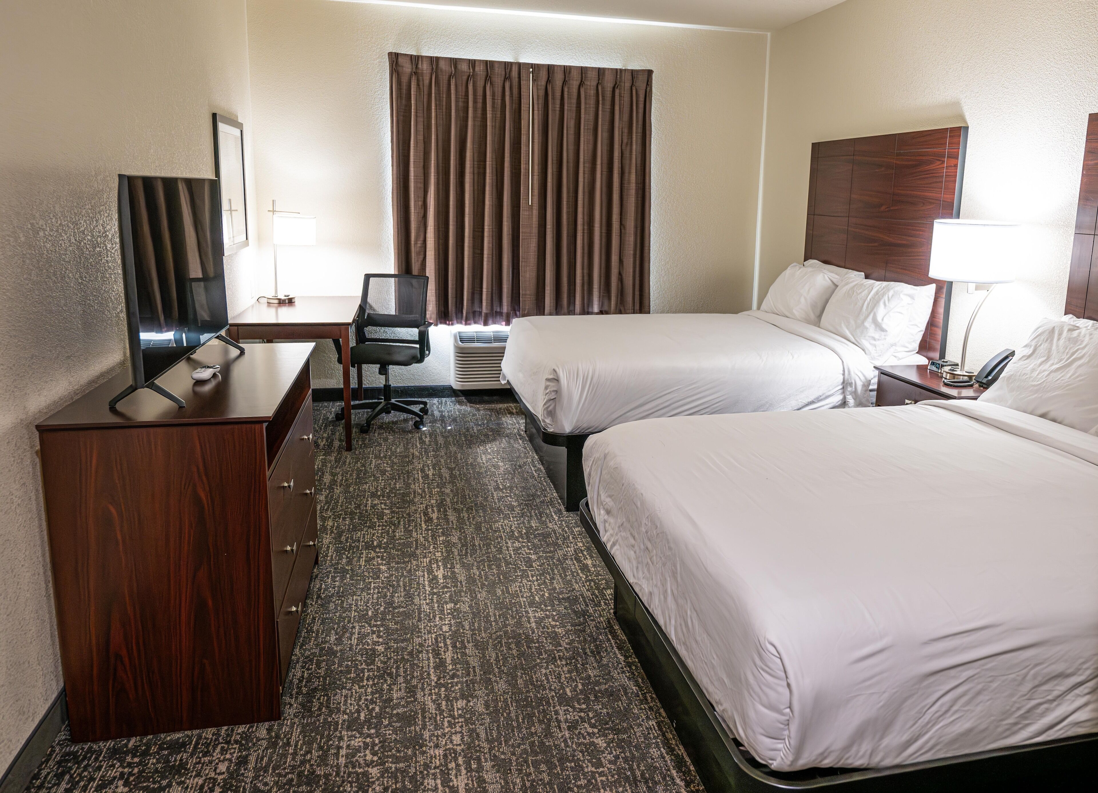Een hotelkamer met twee bedden, een bureau, een stoel, een televisie en een raam met gordijnen.