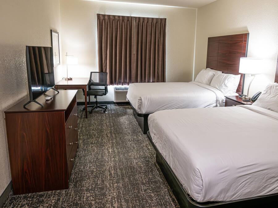 Een hotelkamer met twee bedden, een bureau, een stoel, een televisie en een raam met gordijnen.