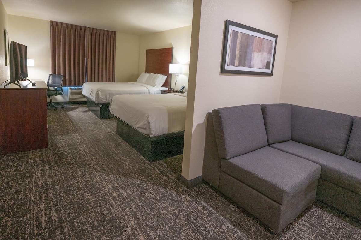 A hotel room with two beds, a gray sofa, a desk, and a framed picture on the wall.