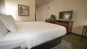 Quarto de hotel com uma cama grande, uma televisão sobre um suporte de madeira, uma escrivaninha pequena e um quadro emoldurado na parede.