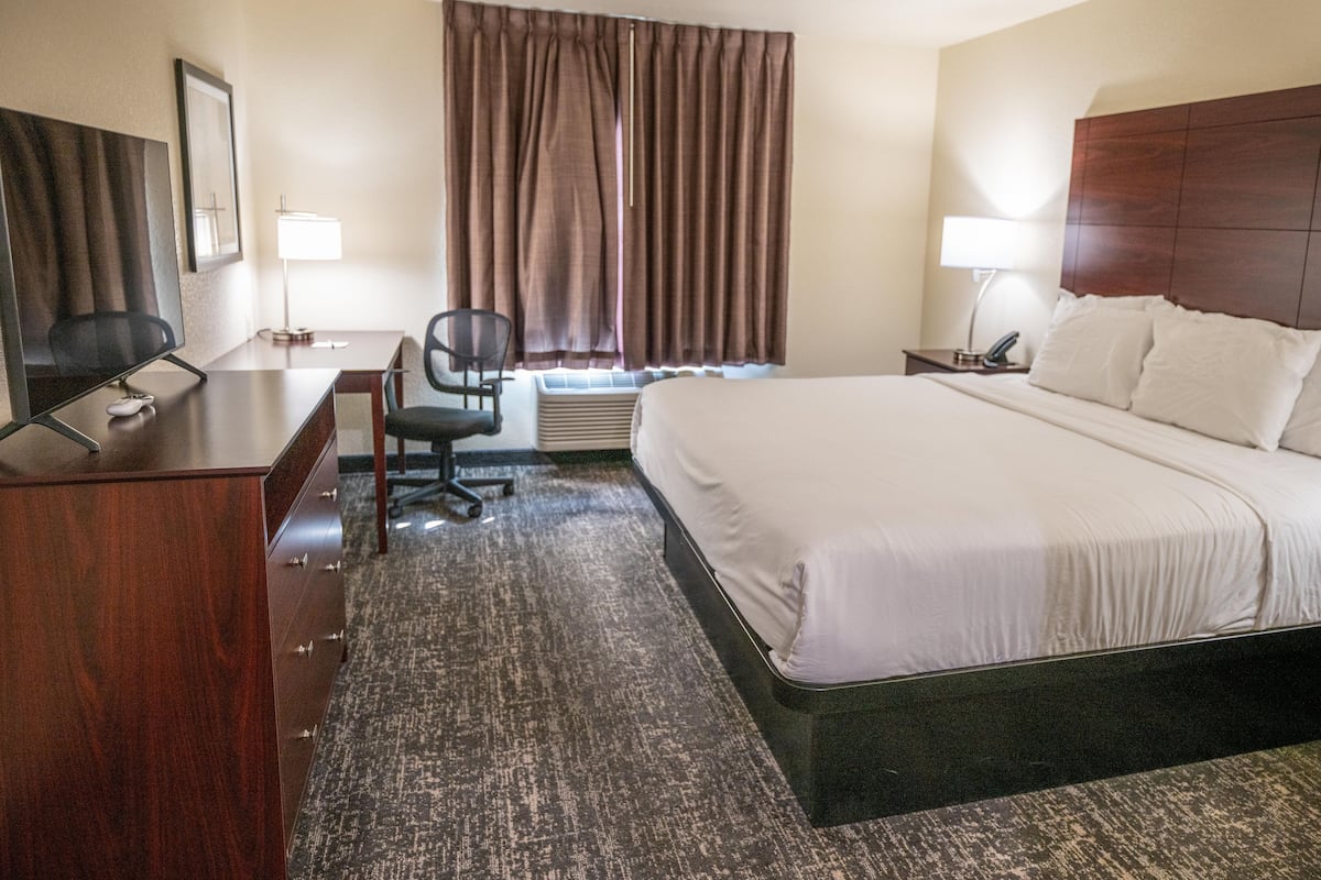 A hotel room with a bed, desk, chair, and a television.