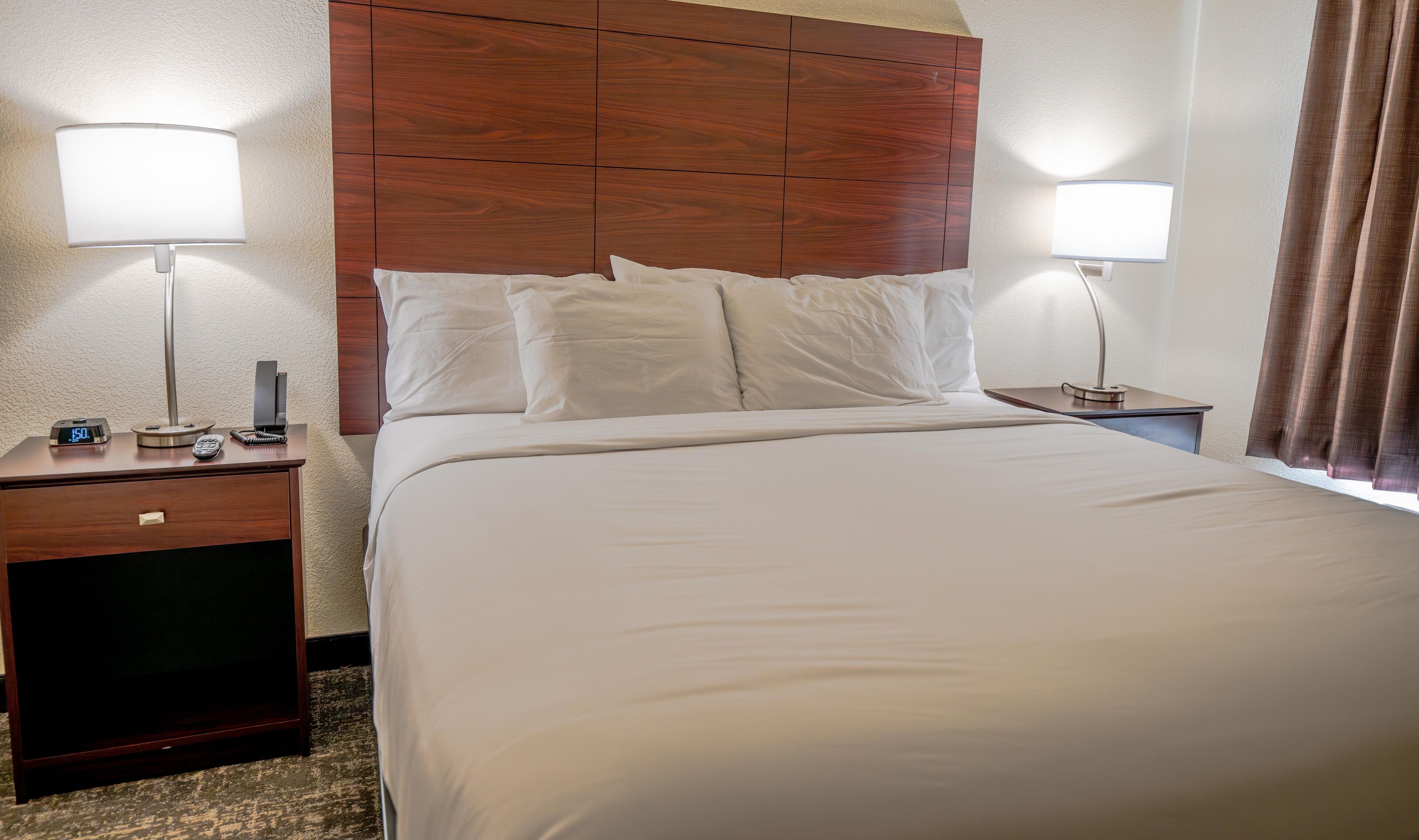 A hotel room with a large bed, two bedside tables, a wooden headboard, and two wall-mounted lamps.