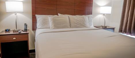 A hotel room with a large bed, two bedside tables, a wooden headboard, and two wall-mounted lamps.