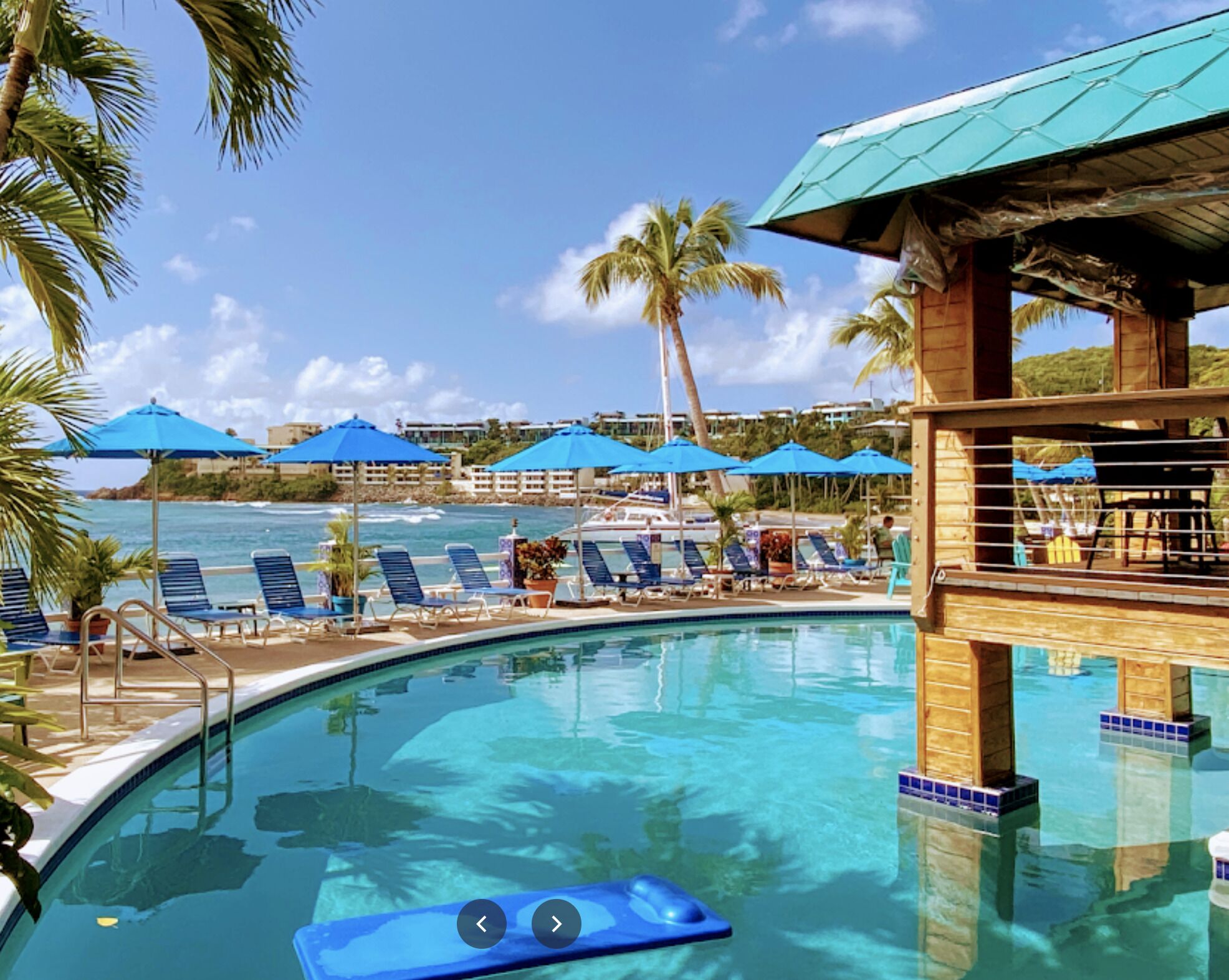 A pool area with lounge chairs and umbrellas, a view of the ocean, and a wooden structure.