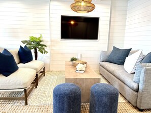 A living room with a sofa, armchair, ottoman, coffee table, and a TV mounted on the wall.