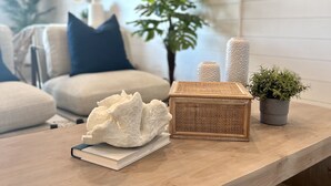 Une table en bois sur laquelle se trouvent un livre, un objet blanc, une boîte en osier et une plante en pot.