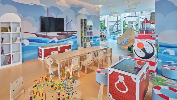 Un área de juegos infantiles con un mural de un barco, un tobogán y una casita.