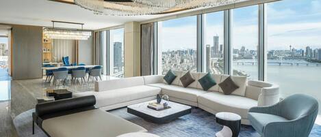 A modern living room with a large sofa, a coffee table, and a view of a cityscape through large windows.