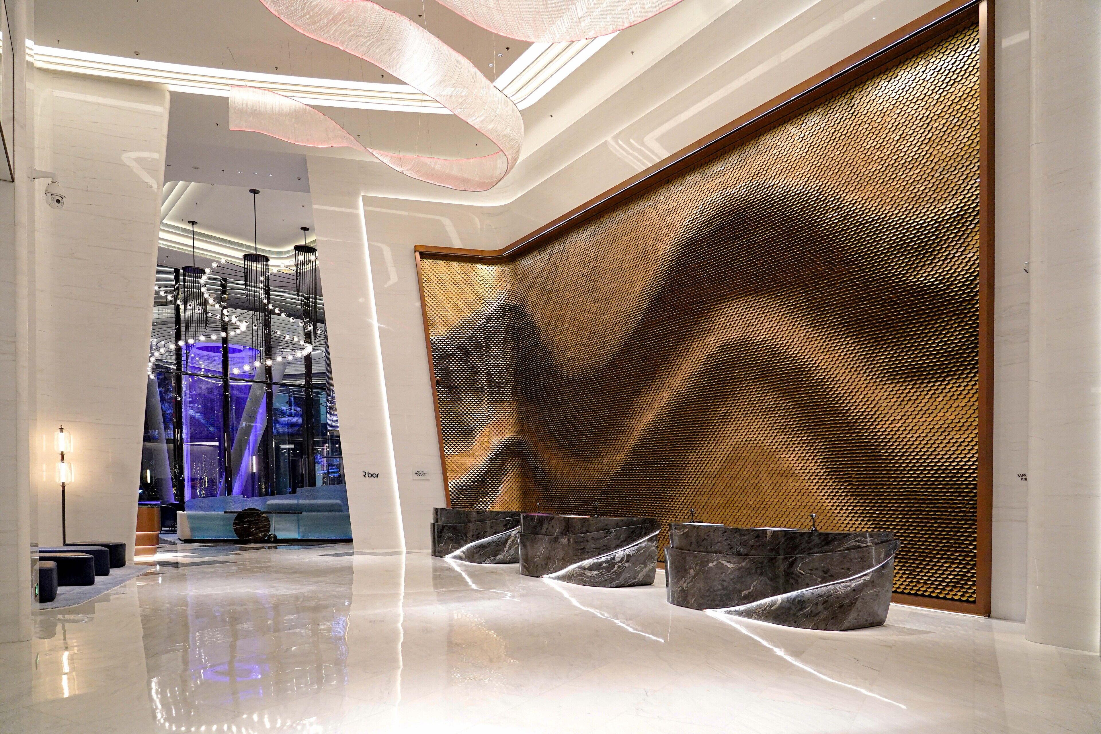 Un hall d’entrée moderne doté d’un sol réfléchissant, d’un espace détente avec des fauteuils noirs et d’un mur décoratif à motifs texturés.
