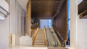 Un interior moderno con una escalera central, barandales de vidrio y techo de listones de madera.