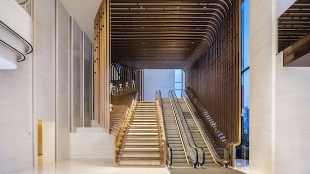 Een modern interieur met een centrale trap, begrensd door glazen leuningen en een houten lambrisering.