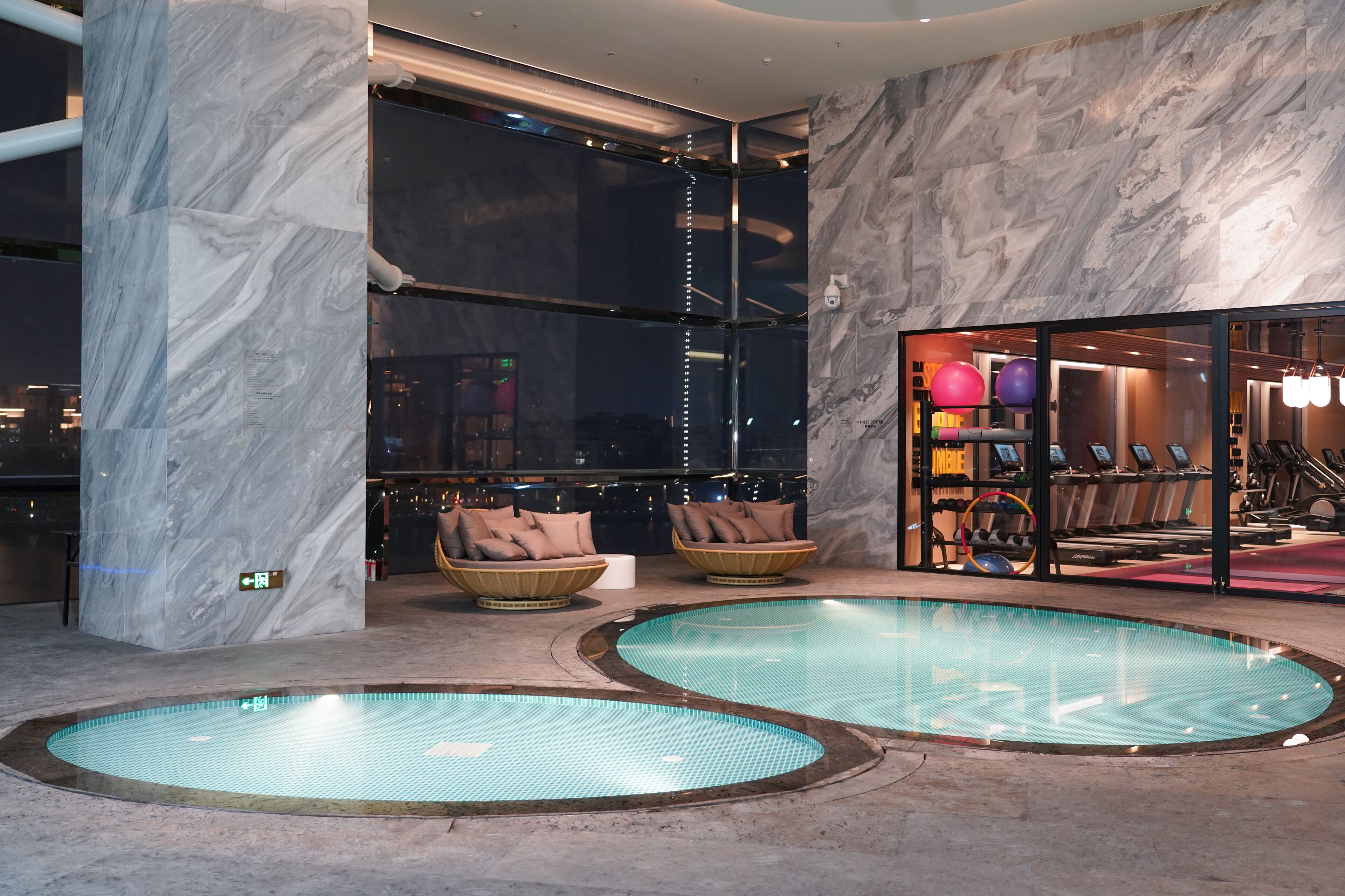 A modern indoor pool area with marble walls and two seating areas.