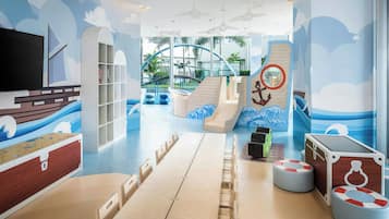 Children can play and learn in this nautical-themed play area with a table, chairs, TV, bookshelf, and play structures.