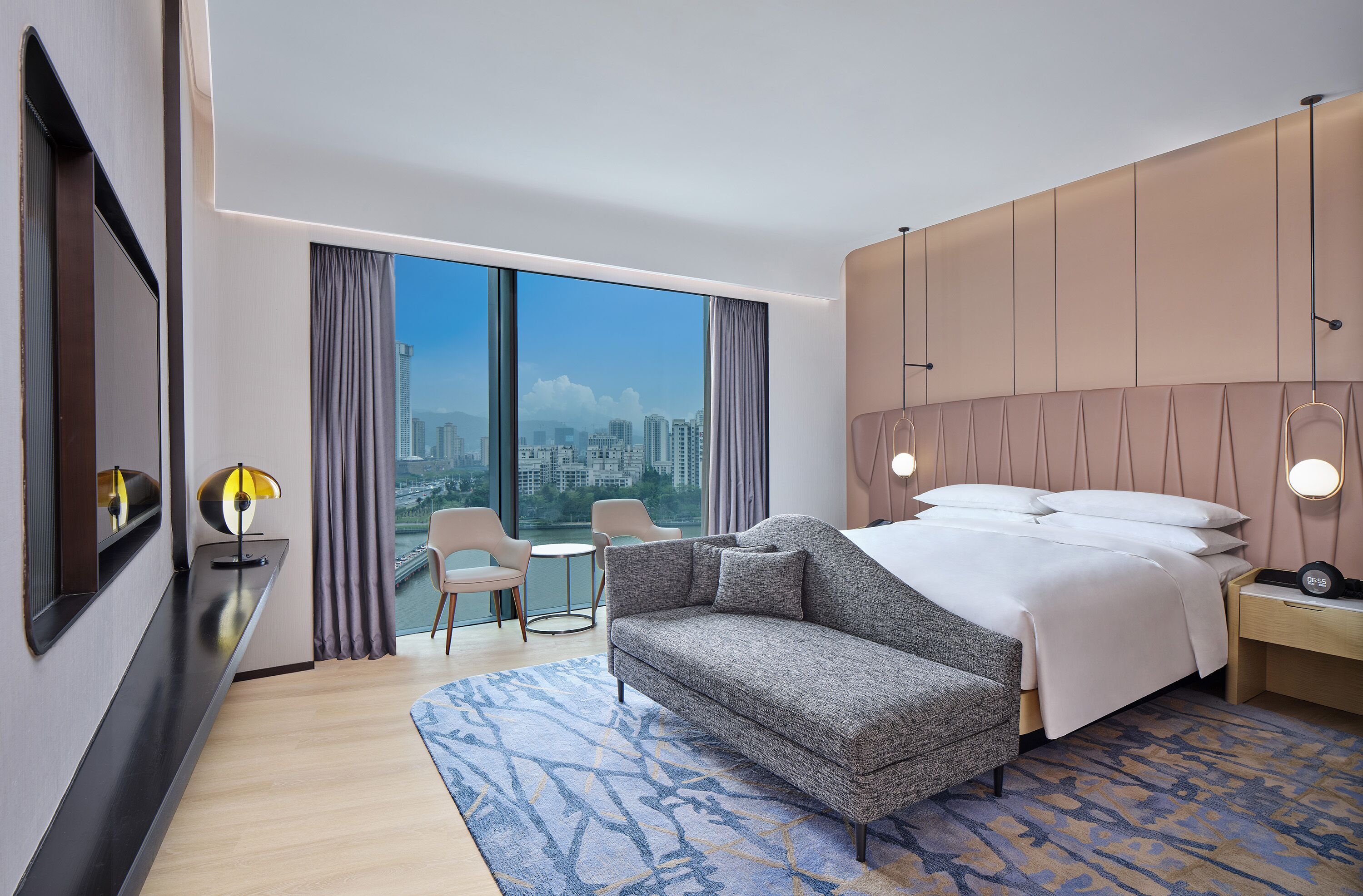 A modern hotel room with a large bed, a sofa, a small table, and a chair.