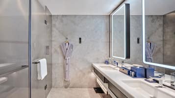 Un baño moderno con cabina de ducha de vidrio, dos lavamanos y un espejo grande.