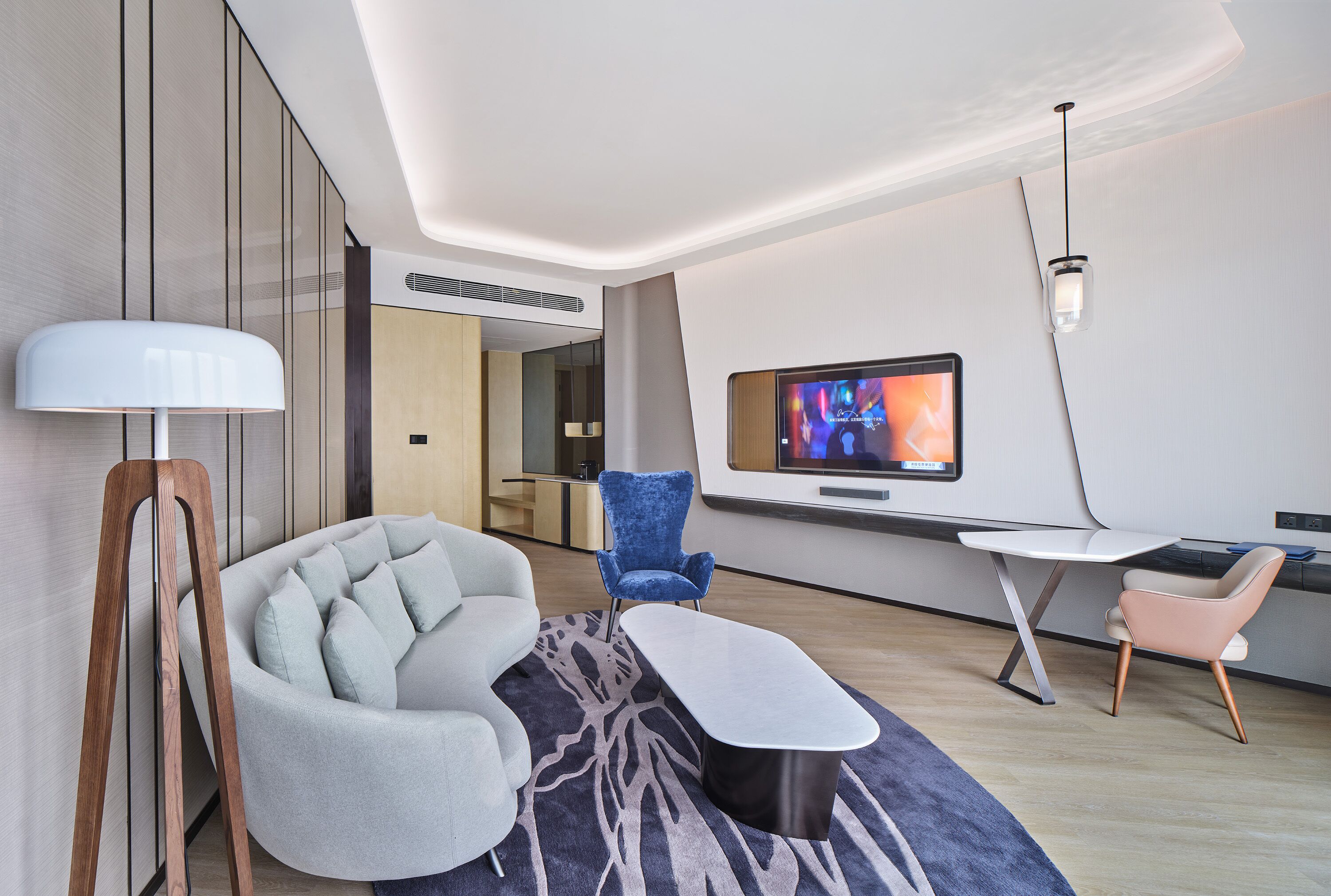 A modern living room with a sofa, a blue armchair, a coffee table, and a TV mounted on the wall.