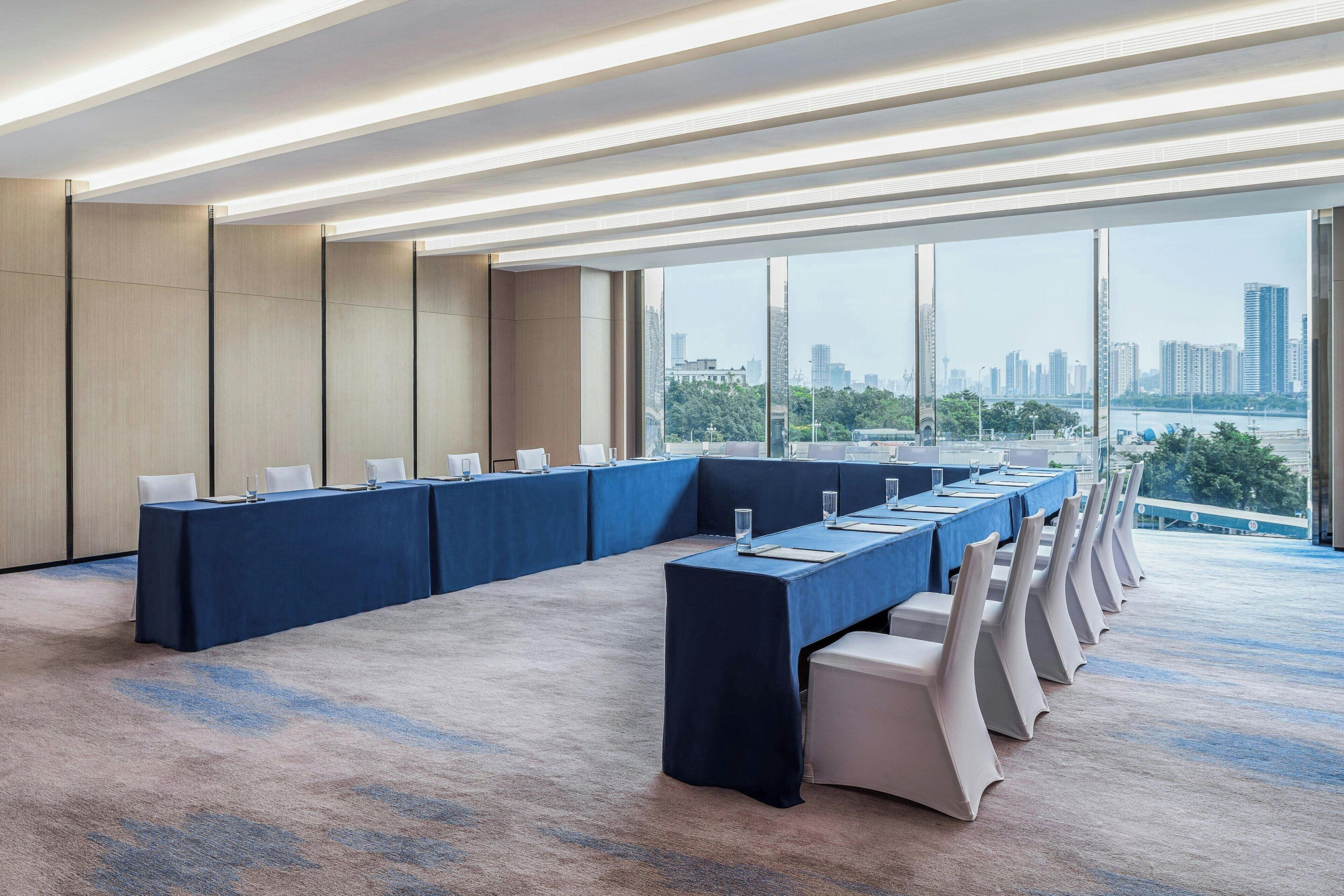 A conference room with a long table, white chairs, and large windows offering a city view.