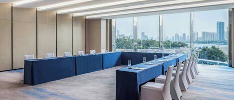 A conference room with a long table, white chairs, and large windows offering a city view.