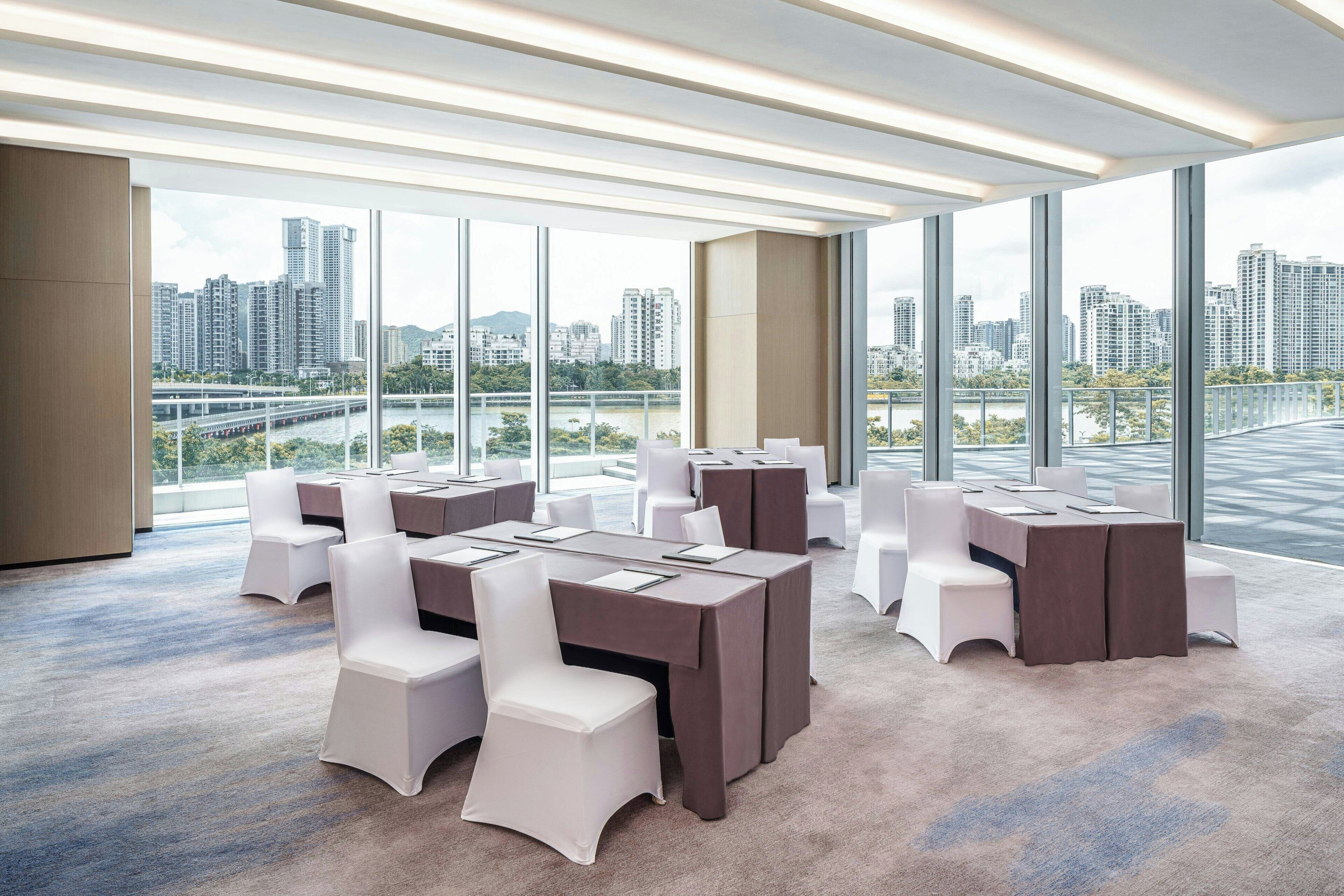A modern conference room with large windows, multiple tables, and white chairs.