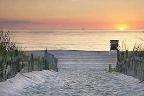 Ein Strandweg führt zu einer Bank mit Blick auf den Sonnenuntergang über dem Meer.