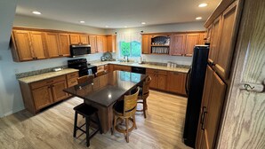 Une cuisine moderne avec des meubles en bois, des plans de travail en granit, un îlot central doté de tabourets et des appareils électroménagers intégrés.