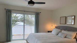 Une chambre dotée d’un grand lit, d’un ventilateur de plafond, d’une table de chevet avec une lampe et offrant une vue sur l’extérieur grâce à une porte coulissante.