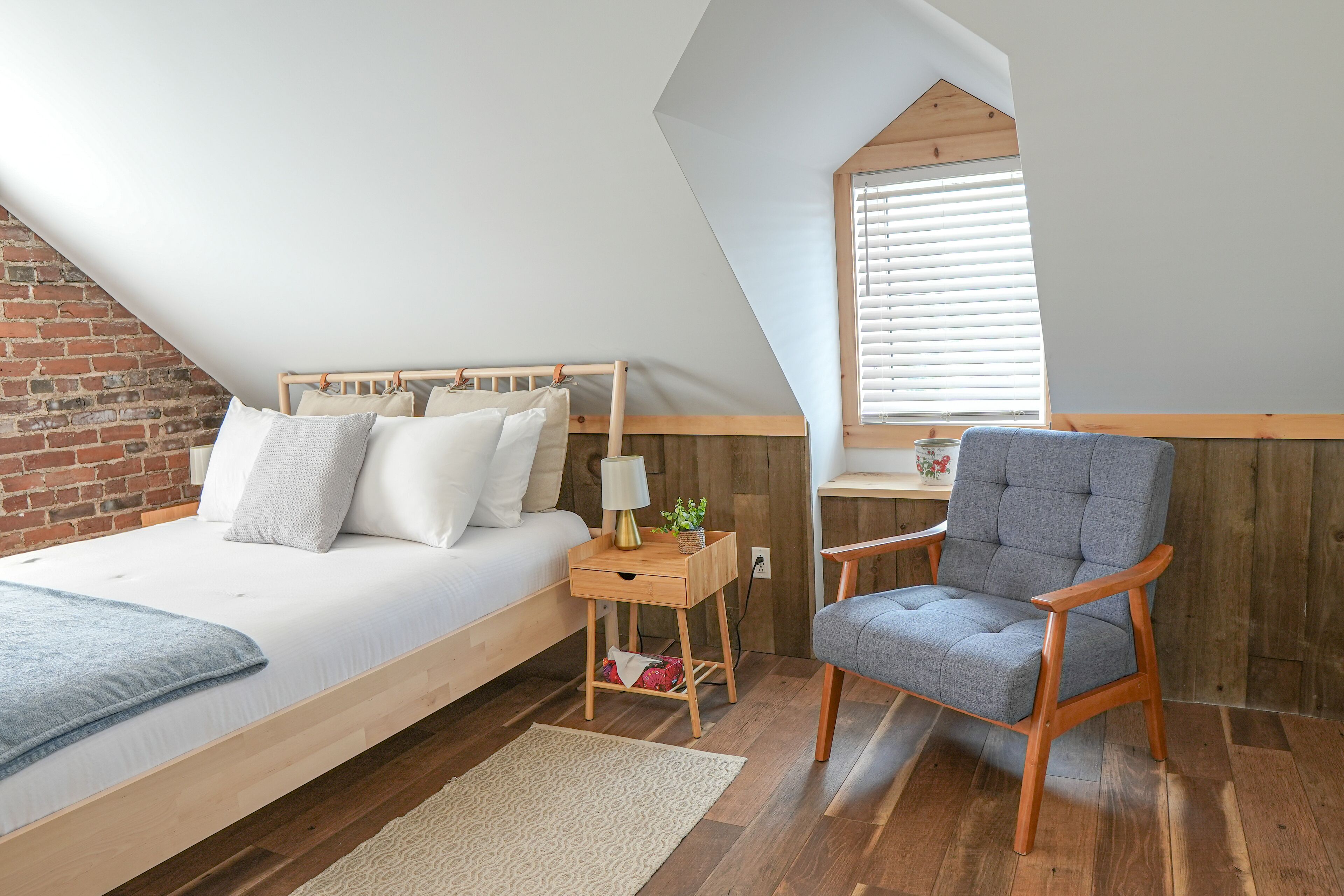 Een slaapkamer met een hoogslaper, een houten nachtkastje, een stoel en een raam met jaloezieën.